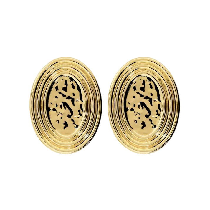A pair of gold oval stud earrings with concentric ridged outer edges and a textured, openwork patterned center, shown on a light cream background.